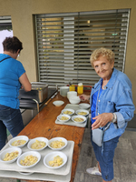 Eine ältere Frau steht an einem Tisch mit mehreren Schüsseln voller Essen.
