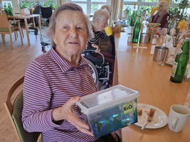 Eine Seniorin hält eine transparente Box mit buntem Inhalt in der Hand.