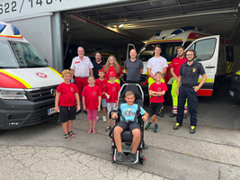 Gruppe von Kindern und Rettungskräften vor einem Rettungswagen, ein Kind sitzt im Rollstuhl.