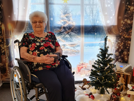 Eine ältere Frau im Rollstuhl sitzt vor einem weihnachtlichen Fenster.