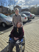 Eine junge Frau steht hinter einer älteren Frau im Rollstuhl.