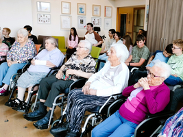 Ältere Menschen in Rollstühlen sitzen zusammen und hören einer Präsentation zu.