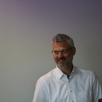 Geschäftsführer Oliver Löhlein steht in weißem Hemd und mit Brille vor einer Wand.