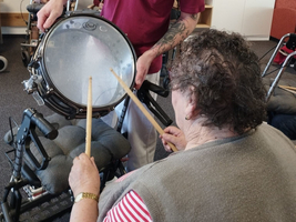 Ein Betreuer zeigt einem Bewohner, wie man auf eine Trommel spielt.