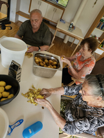 Drei ältere Menschen schälen gemeinsam Kartoffeln an einem Tisch.