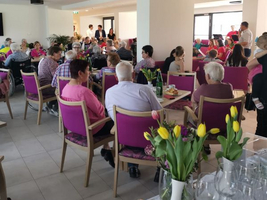 Menschen sitzen in einem lichtdurchfluteten Raum und genießen ein gemeinsames Essen.