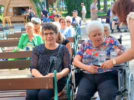 Zwei Frauen sitzen entspannt im Freien, eine wird von einer Bedienung mit Getränken bedient.