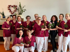 Eine Gruppe von Frauen in roten Arbeitskleidungen hält Blumen in der Hand.