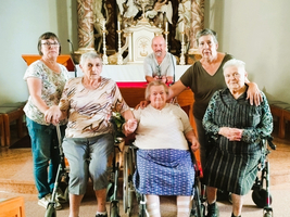 Sechs Personen stehen und sitzen in einer Kirche, lächelnd und zusammen.