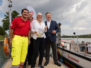 Die Bootseinweihung des Samariterbund Bootes Susanne mit der Präsidentin vom Smariterbund die eine Sektflasche in der Hand hält und noch drei weiteren Personen des Samariterbundes.