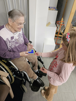 Ein Kind überreicht einer Seniorin ein buntes, herzförmiges Objekt.