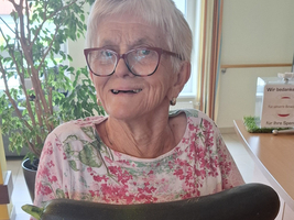 Eine ältere Frau hält große Zucchini und Auberginen in den Händen.