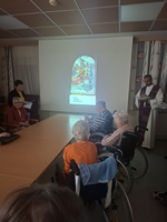 Eine Gruppe älterer Menschen sitzt in einem Raum und verfolgt eine Präsentation.
