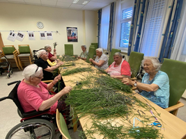 Ältere Frauen basteln gemeinsam mit duftenden Kräutern an einem Tisch.