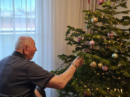 Ein älterer Mann schmückt einen Weihnachtsbaum im Wohnraum.