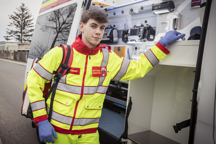 Ein Sanitäter in gelber Uniform steht an einem Krankenwagen.