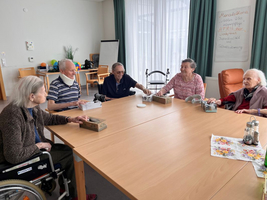 Fünf Senioren sitzen an einem Tisch, beschäftigen sich mit verschiedenen Aktivitäten.