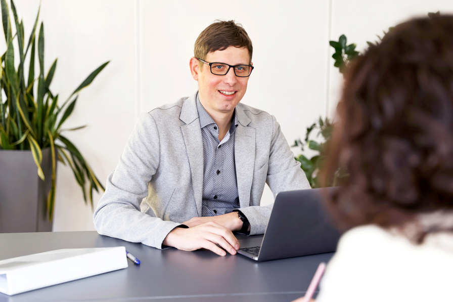 Eine lächelnde Person mit einem Laptop berät eine andere Person zum Thema 24-Stunden-Betreuung.