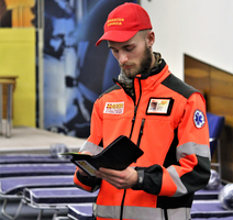 Ein Rettungssanitäter in orangefarbener Uniform liest aufmerksam in einem Notizbuch.