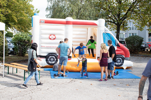Bunte Hüpfburg in Form eines Lieferwagens mit spielenden Kindern und Erwachsenen.