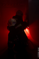 Zwei Feuerwehrleute arbeiten in einem roten, rauchigen Umfeld.