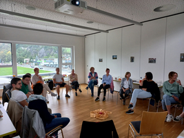 Eine Gruppe von Menschen sitzt im Kreis in einem hellen Raum.
