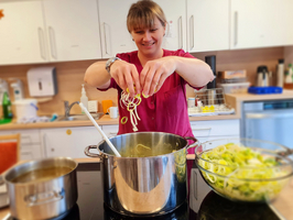 Frau fügt frisch geschnittene Zwiebeln zu einem großen Kochtopf hinzu.