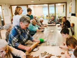 Ältere Menschen und Kinder backen gemeinsam Kekse am Tisch.