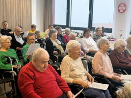 Senioren sitzen in einem Raum und singen zusammen, während sie Texte in der Hand halten.