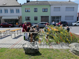 Ältere Menschen unterhalten sich im Freien, umgeben von Bänken und bunten Zweigen.