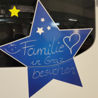 Blaue Sternform mit weißen Sternen und einem lächelnden Gesicht. Darauf steht in geschwungener Schrift: 