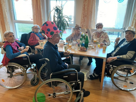 Sechs Senioren in Rollstühlen sitzen um einen Tisch und genießen Getränke und Snacks.