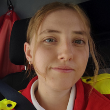 Eine Person mit rot-gelber Bekleidung sitzt im Fahrzeug und lächelt.