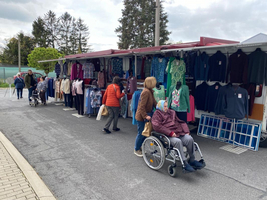 Kleidermarkt mit verschiedenen Auslagen und Besuchern, darunter eine ältere Frau im Rollstuhl.