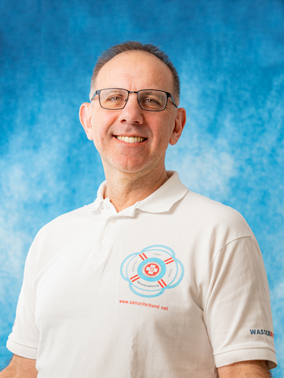 Lächelnder Mann in einem weißen Polo-Shirt mit Wasserrettungs-Logo.