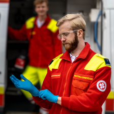 Zwei Notfallsanitäter bereiten sich auf einen Einsatz vor, während sie Schutzkleidung anlegen.
