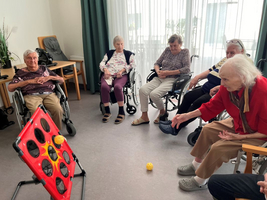 Ältere Menschen im Rollstuhl spielen zusammen mit einem gelben Ball.