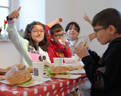 vier Kinder sitzen an einem Tisch und essen Burger, Generationenausflug