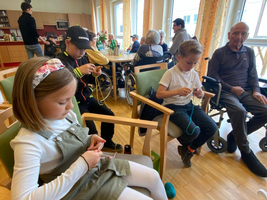Kinder und Senioren sitzen zusammen und handarbeiten in einem Gemeinschaftsraum.