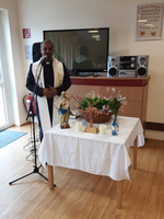 Ein Priester steht neben einem Tisch mit religiösen Symbolen und Blumen.