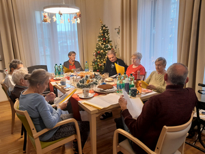 Die Bewohner:innen unserer Senior:innen-WG feiern gemeinsam gemütlich Weihnachten. Sie sitzen gemeinsam an einem großen Tisch, hinter ihnen steht ein geschmückter Christbaum.
