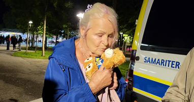 Eine ältere Frau umarmt einen Teddybär und lächelt dabei.