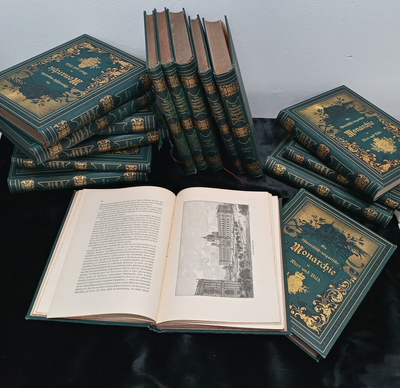 Eine offene Buchseite neben mehreren geschlossenen, gebundenen Büchern zum Thema Monarchie.