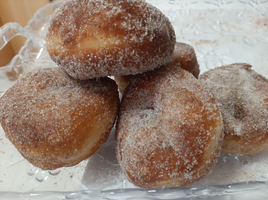 Fünf zuckerbestreute Krapfen auf einem glänzenden Teller.