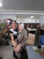 Zwei Frauen tanzen fröhlich mit lustigen Hüten in einem Gemeinschaftsraum.