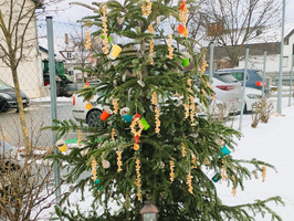 Ein geschmückter Weihnachtsbaum steht im Schnee mit bunten Dekorationen und Geschenken.