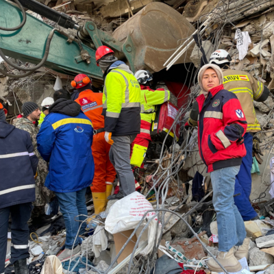 Personen suchen mithilfe von Bagger nach Verschütteten in Trümmern