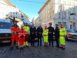 Eine Gruppe von zwei Frauen und sieben Männern stehen vor Rettungsfahrzeugen