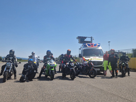 Sechs Motorradfahrer posieren mit einem Einsatzfahrzeug an einem sonnigen Tag.