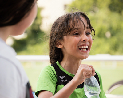 Mädchen in grünem Sportshirt mit Wasserflasche, lacht
